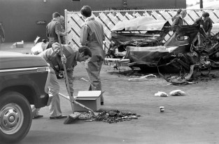 Man sweeping and shoveling debris from an automobile and putting it into a box for investigation purposes. Next to him is an Evansville Fire Department employee, and other law enforcement officials are nearby, some inspecting the mangled remains of the car. Given the location, date, and shape of the car, this is most probably the murder of Ray Ryan, a man in the oil business and a gambler. He went to his health club (Olympia Health and Beauty Resorts, Inc. at 4920 Bellemeade Ave.) the morning of Oct. 18, 1977, and when he came out and started his car, it exploded. The murder was not solved, but is widely believed to have been a mob hit, 1977. Source: University Archives and Special Collections, MSS 038-1729.